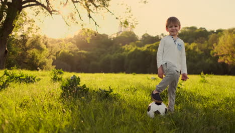 Boy-standing-with-a-football-in-the-summer-at-sunset-looking-at-the-camera.